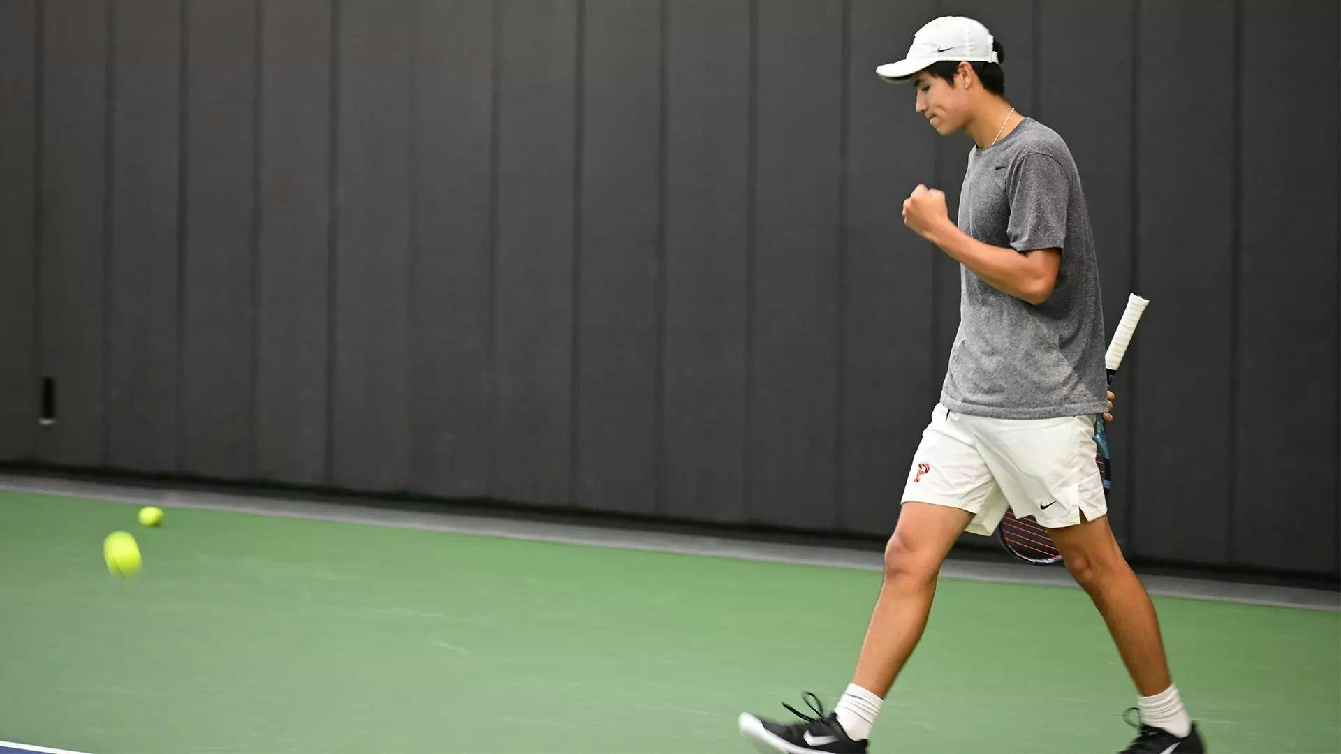 Tennis player in grey shirt and white hat shakes his fist.