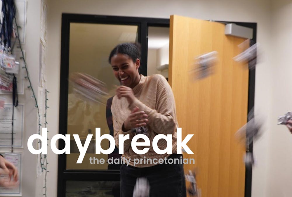 In the for-ground, text reads daybreak. Woman in sweater smilingly braces herself as blurry balls of paper are tossed at her. Door is slightly ajar, name tags hang on hook.