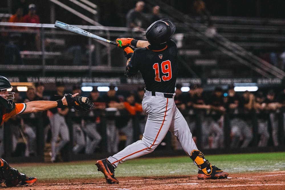 A baseball player in a black jersey swings a bat.