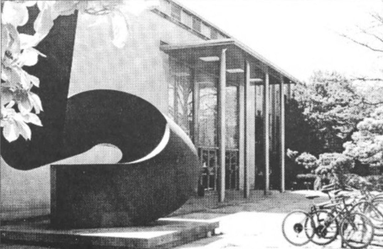 A black and white photograph of the entrance to the E-Quad with bikes parked in front and the “Uroda” statue by Ursula von Rydingsvard. 