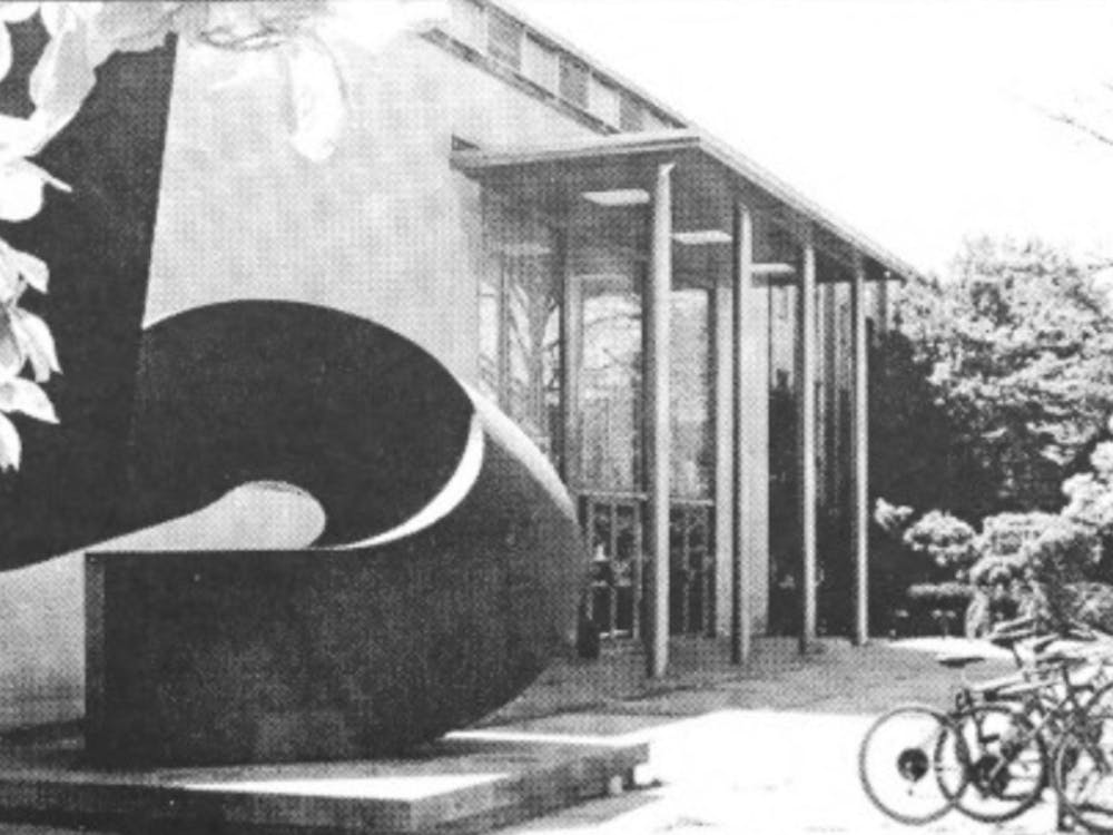 A black and white photograph of the entrance to the E-Quad with bikes parked in front and the “Uroda” statue by Ursula von Rydingsvard.