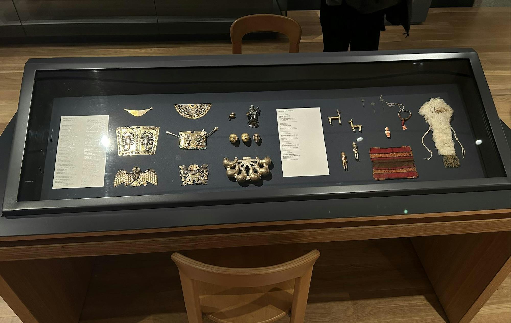 A photo of a table holding several small objects, some metal ornaments and others made of cloth encased in glass. 