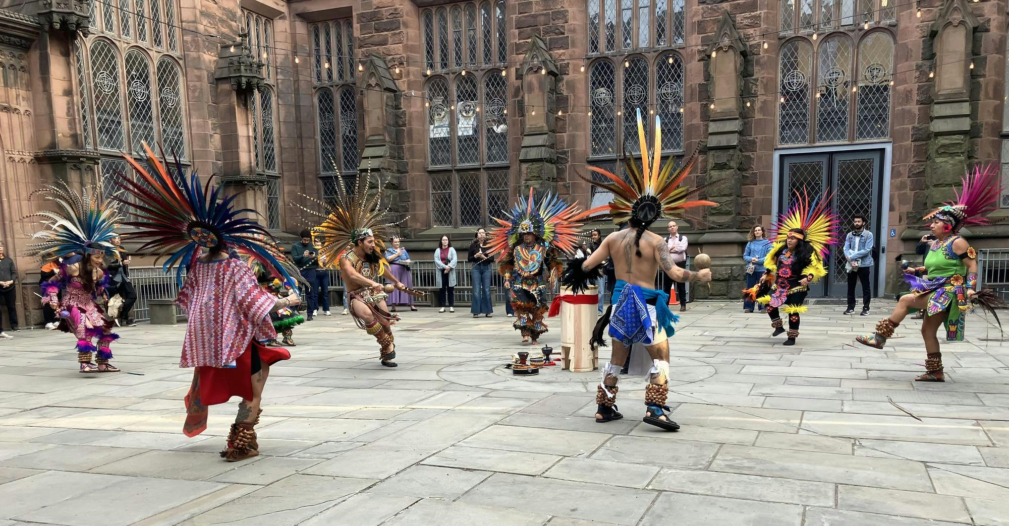 A group of dancers dressed in colorful, traditional Aztec attire dancing around a drummer. 