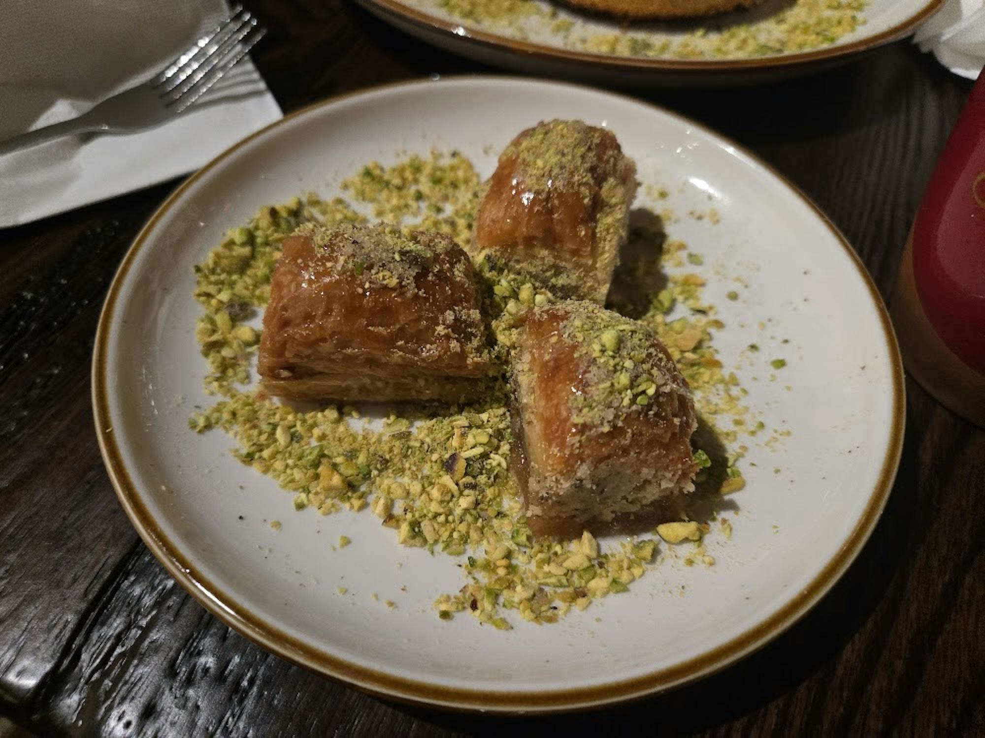 Three pieces of a layered pastry dessert coated with syrup and crushed pistachios.