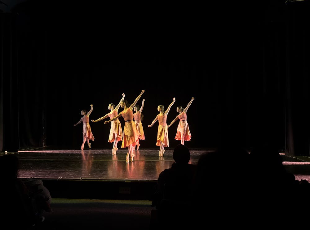 Six ballerinas are in pink outfits on a black stage.