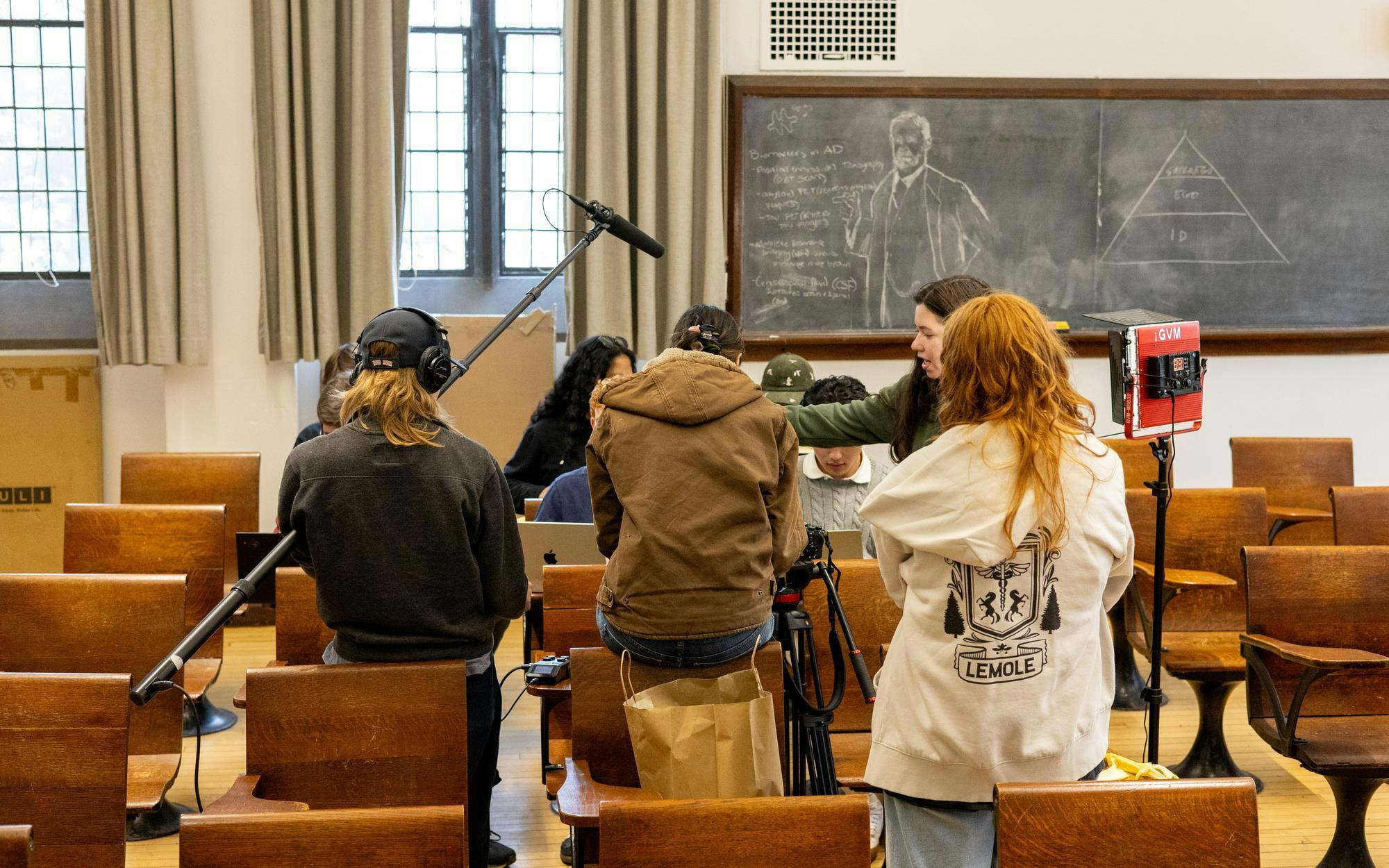 A multitude of students wearing multicolored outfits are working with black cameras and film equipment.