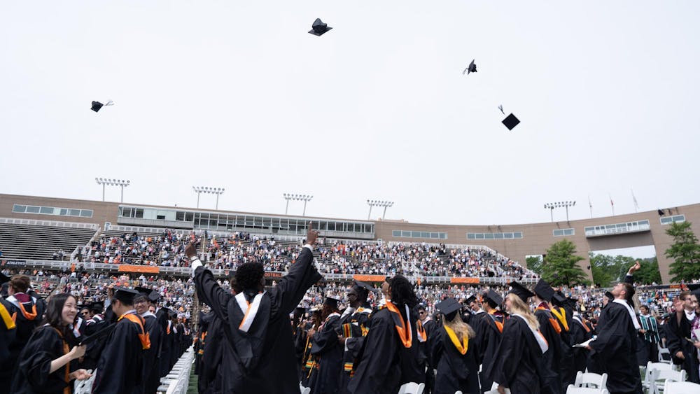 A large group of people wearing long robes throw square caps into the air.