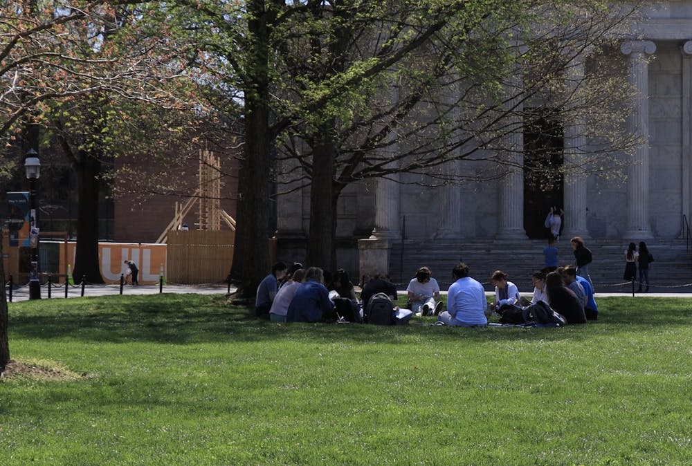 In the shade of a blooming tree, a group of students sit in a circle upon green grass.