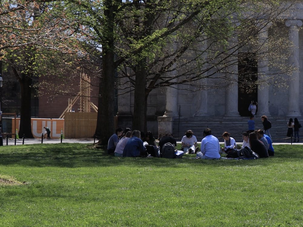 In the shade of a blooming tree, a group of students sit in a circle upon green grass.