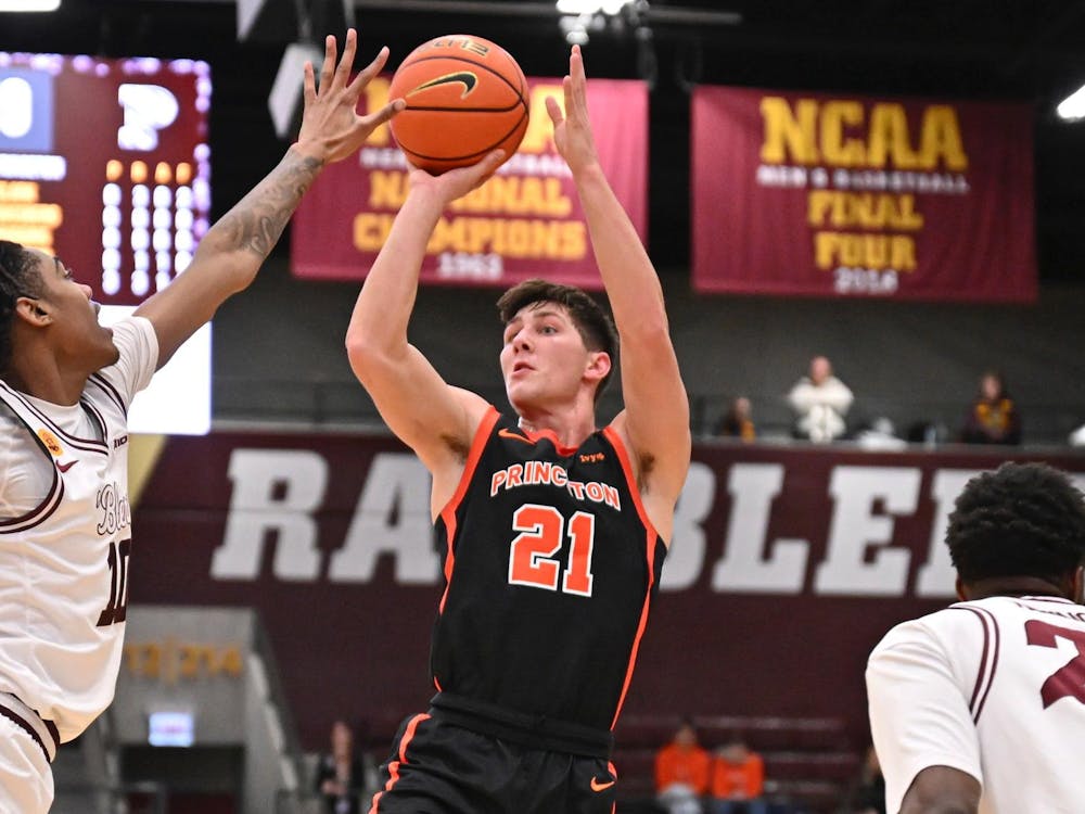 A Princeton basketball player wearing No. 21 takes a jump shot as a Loyola Chicago defender in white contests with banners in the background.