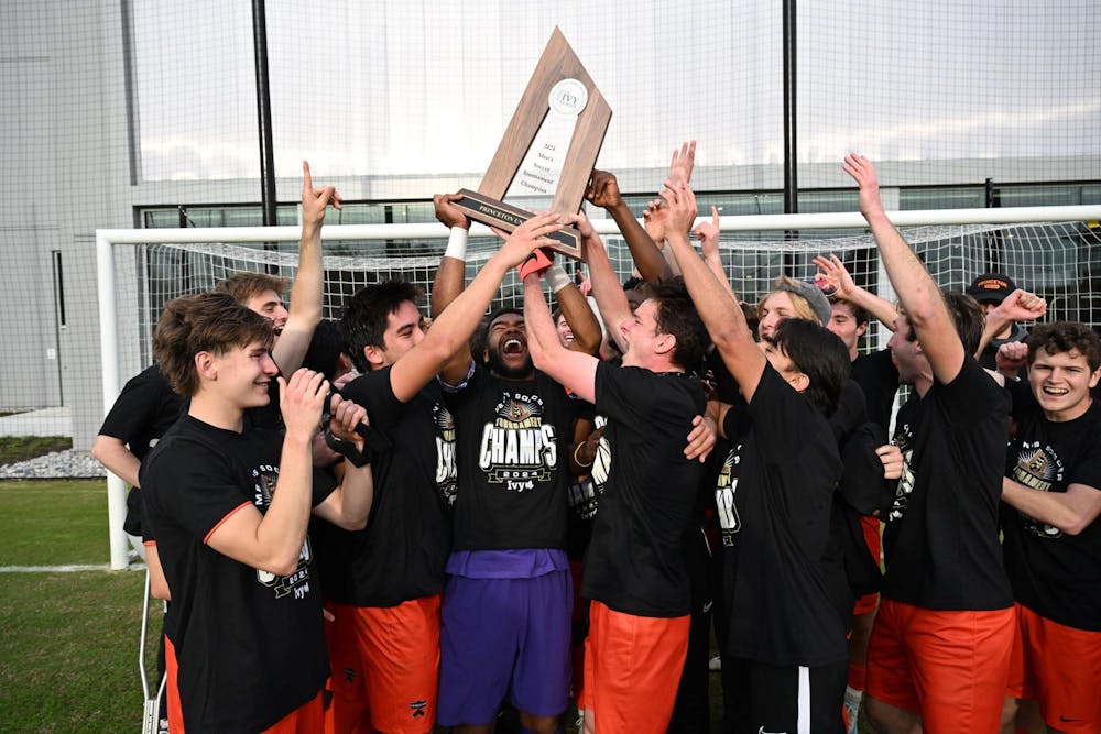 A group of men lifting a trophy together on a grass field.