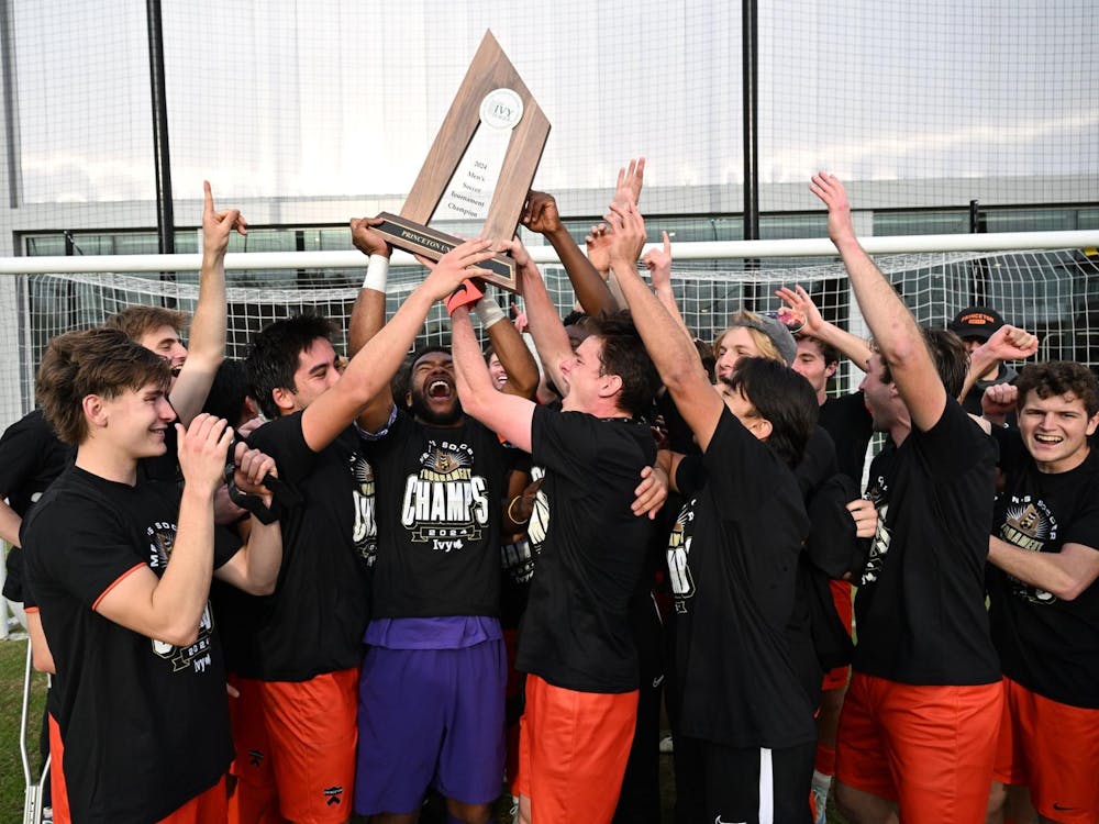 A group of men lifting a trophy together on a grass field.