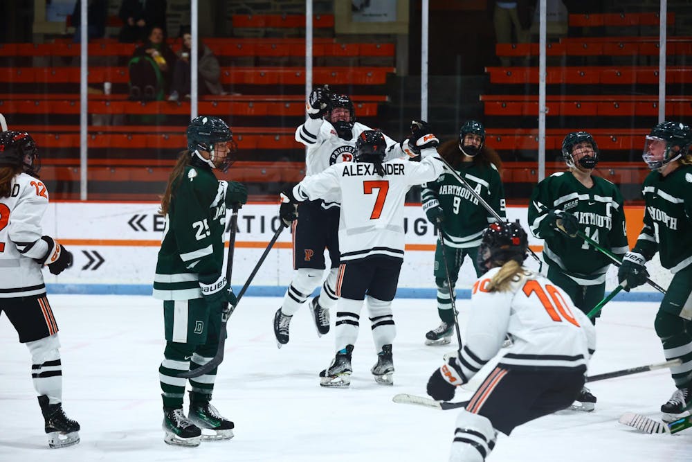 Princeton women's hockey players in white jerseys celebrate a goal on the ice.