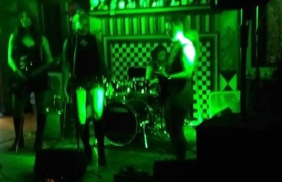 Green lights shine on three shadowy figures, all playing musical instruments.