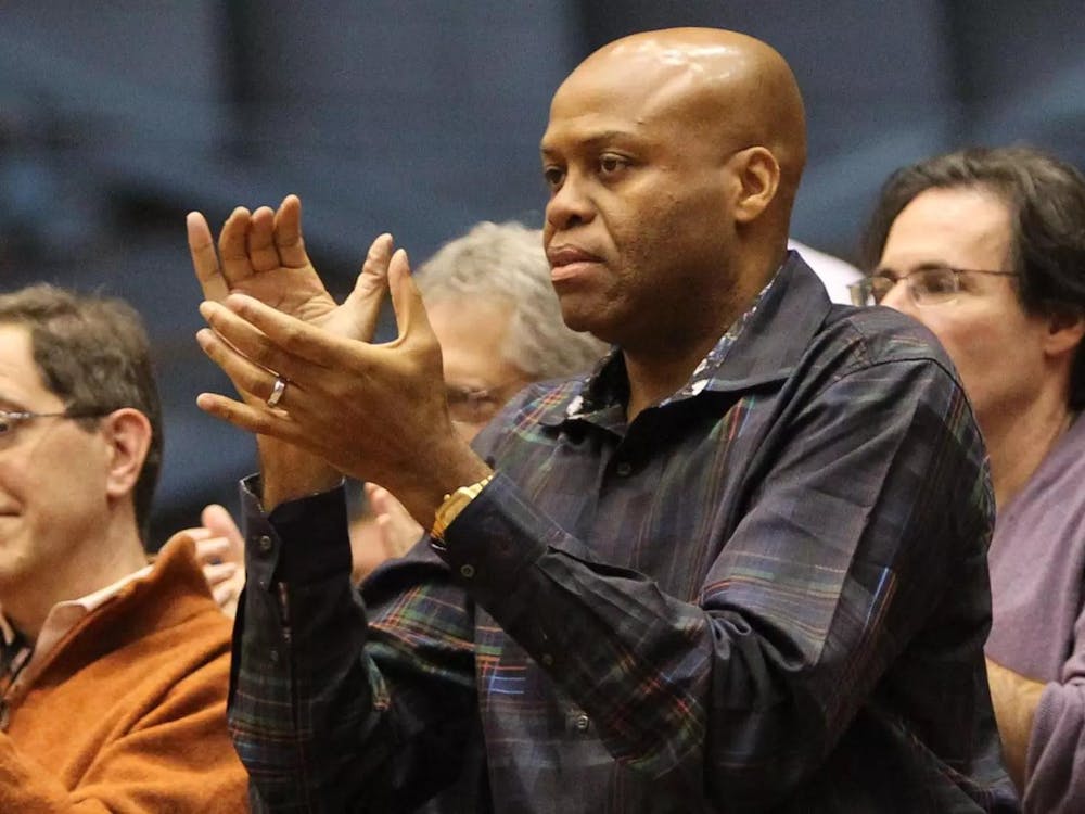 Craig Robinson ’83 stands and applauds in a gymnasium, wearing a dark plaid shirt.