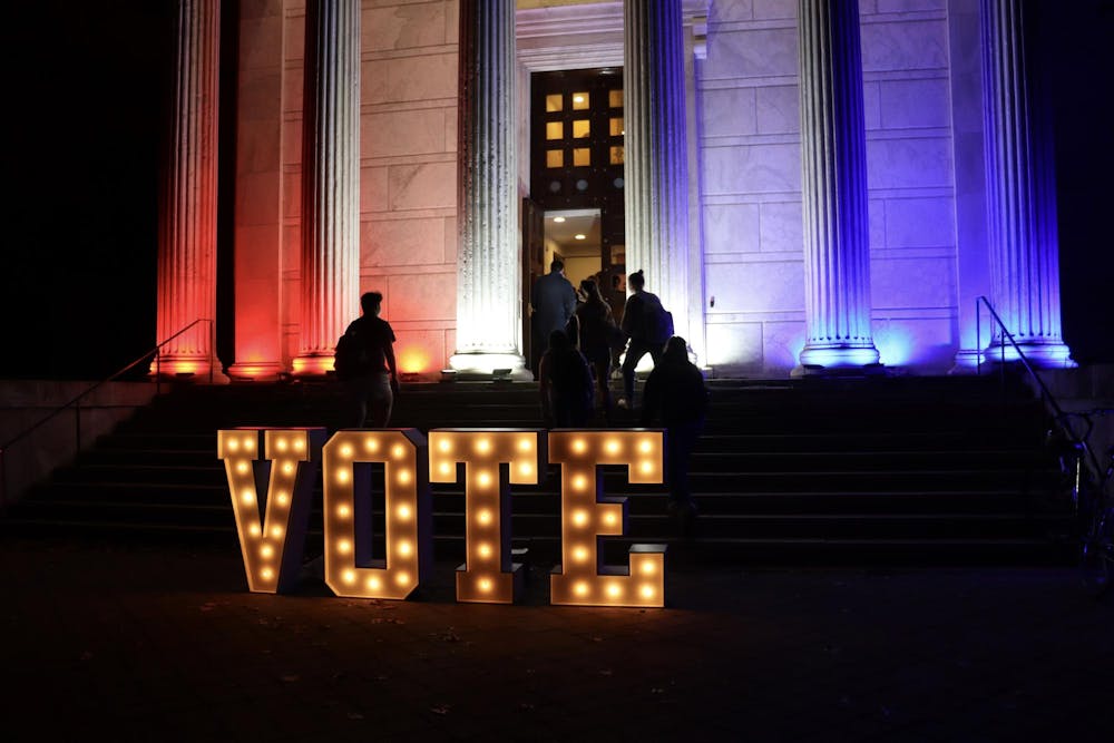 Big sign with “VOTE” in front of a columned building with red and blue lights on the sides.