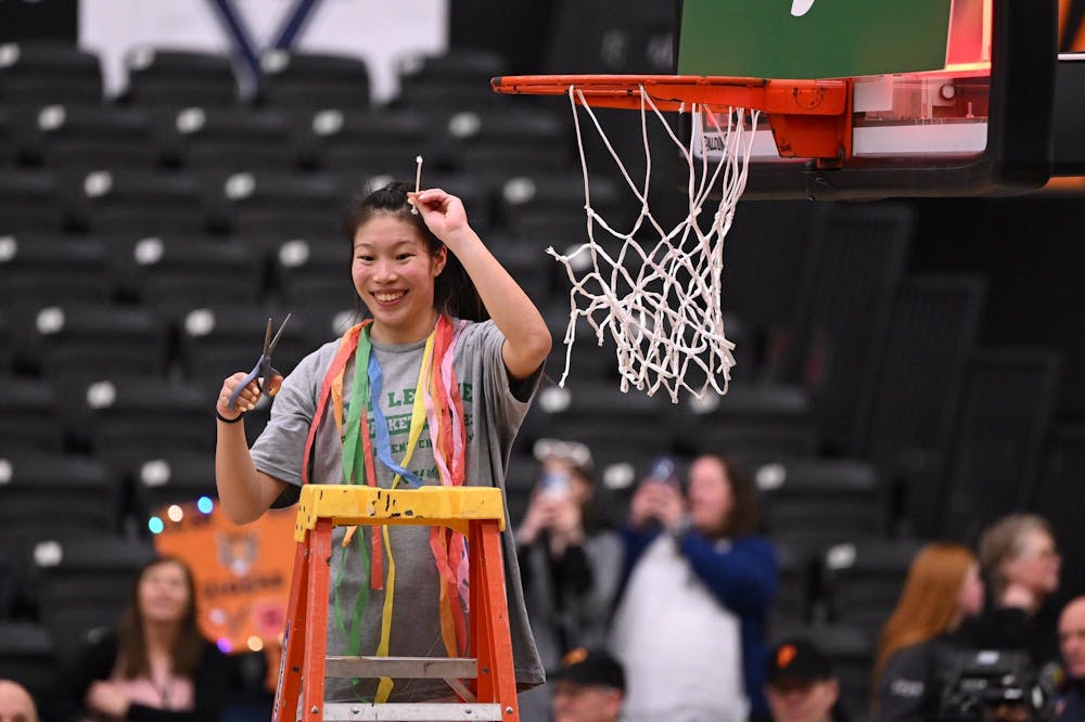 Player on ladder cuts down net, holds up piece of net in celebration. 
