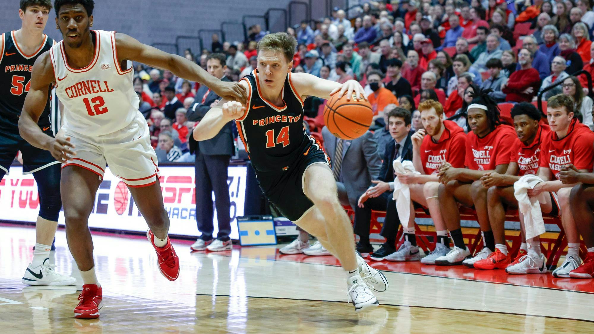 A basketball player runs across the field while another defends against him.