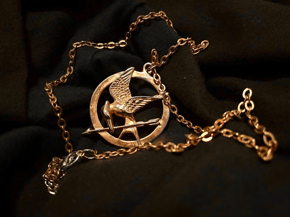 A circular gold pin with a mockingjay in the middle.