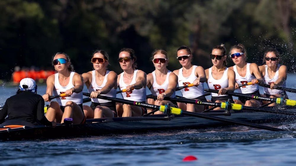 A boat full of women's rowers in white jerseys and sunglasses glides across the water.