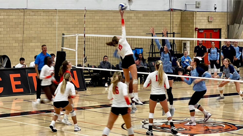 Woman hitting volleyball over net with teammates surrounding her.