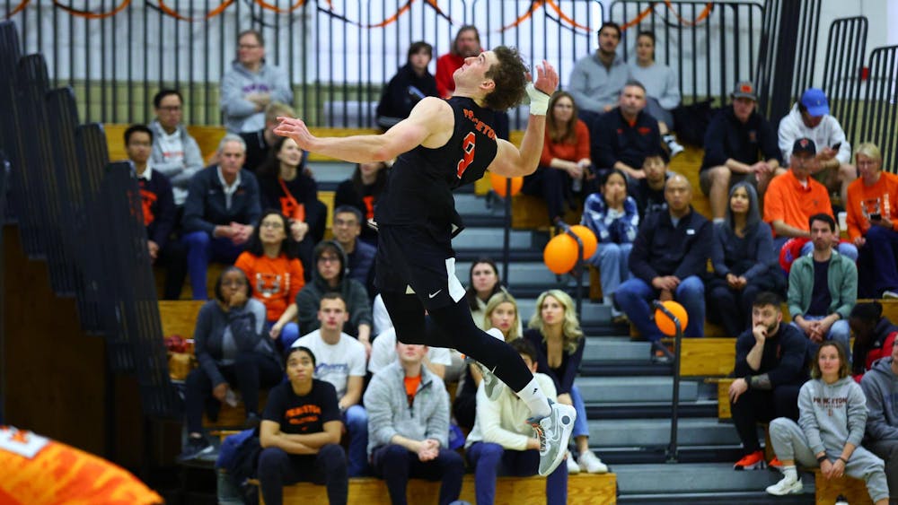 A man jumps up to hit a volleyball in front of a crowd inside a gymnasium. 