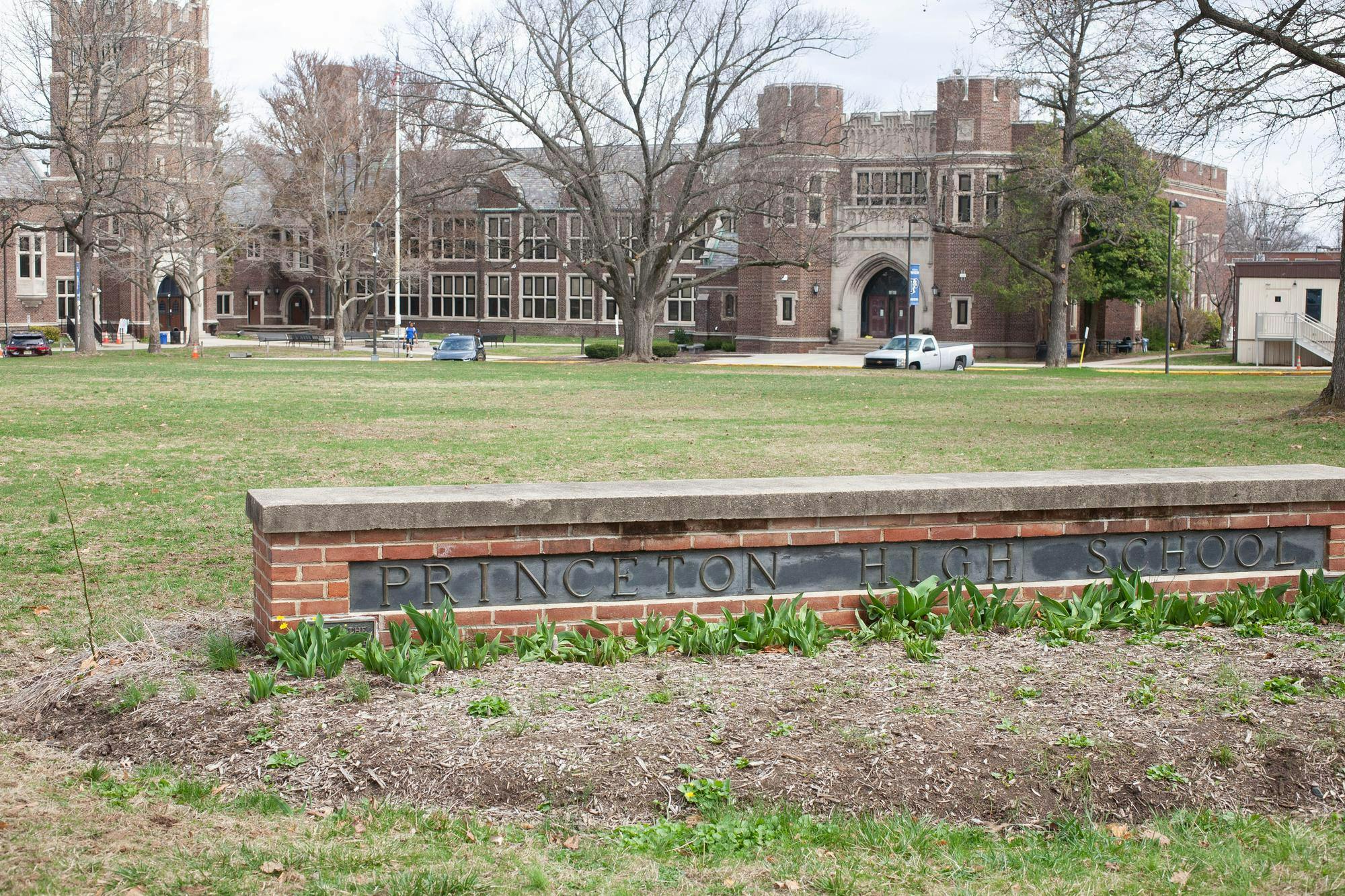 A red-brick building with large windows stands in the background. There is a green field in front of it. In the foreground, there is a brick bench with "Princeton High School" written across it.
