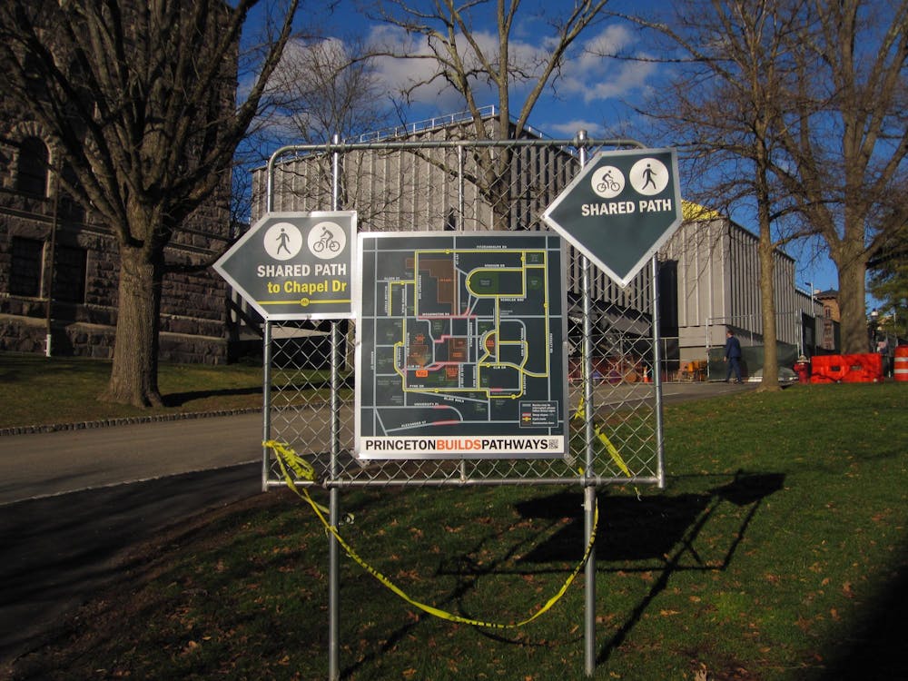 Three signs on a metal grate, with Art Museum construction in the background. The leftmost sign reads "Shared Path to Chapel Dr," the middle sign reads "Princeton Builds Pathways" with a map of the campus, and the rightmost sign reads "Shared Path."
