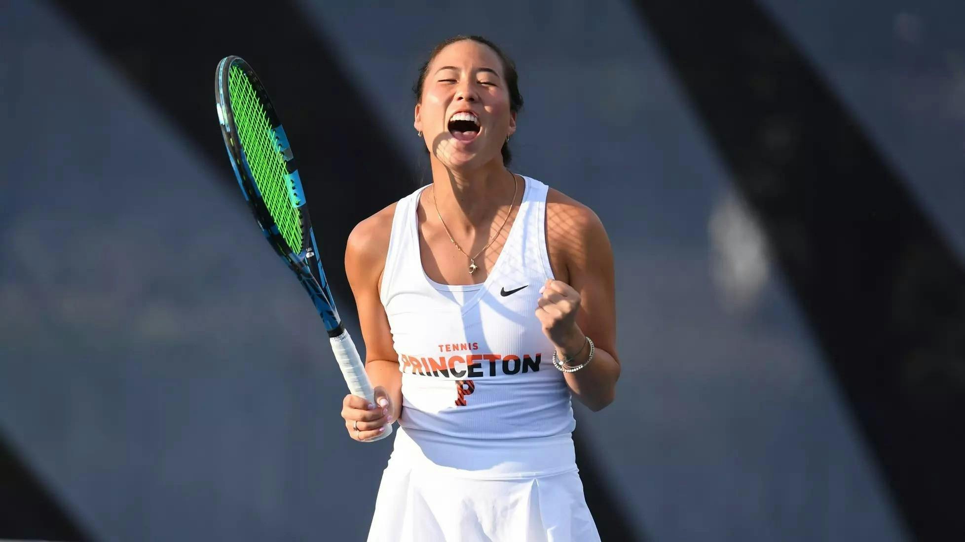 Women's tennis player pumps fists in celebration with a racket in hand after a win.