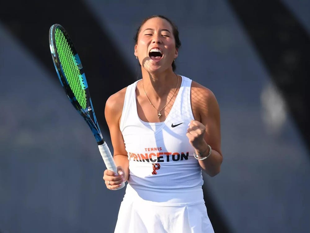 Women's tennis player pumps fists in celebration with a racket in hand after a win.