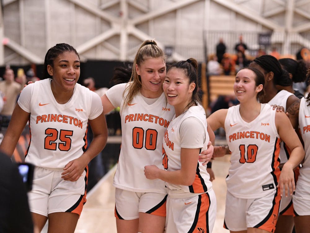 Four women's basketball players in white and orange uniforms gather on a court.