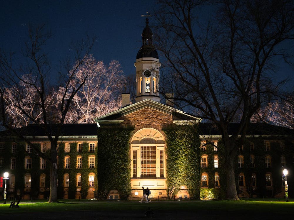 Lights shine up on an old, historical stone building that is covered in ivy at night.
