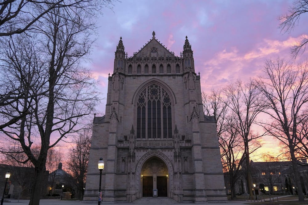 A large stone chapel looms against a sky lit up with blues, pinks, yellows, and purples. 