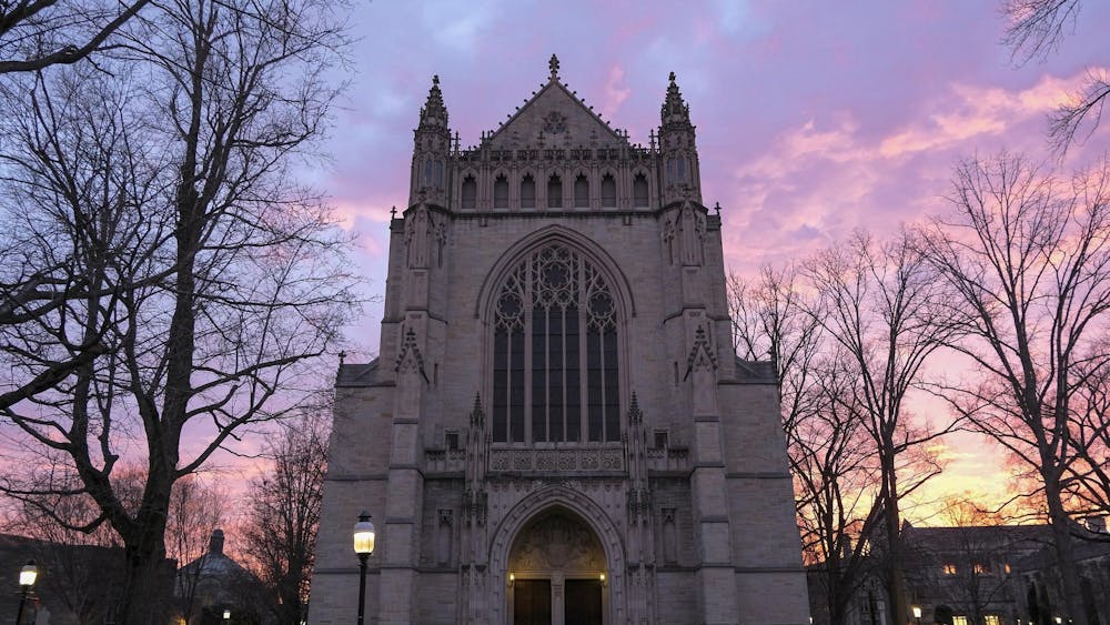 A large stone chapel looms against a sky lit up with blues, pinks, yellows, and purples. 