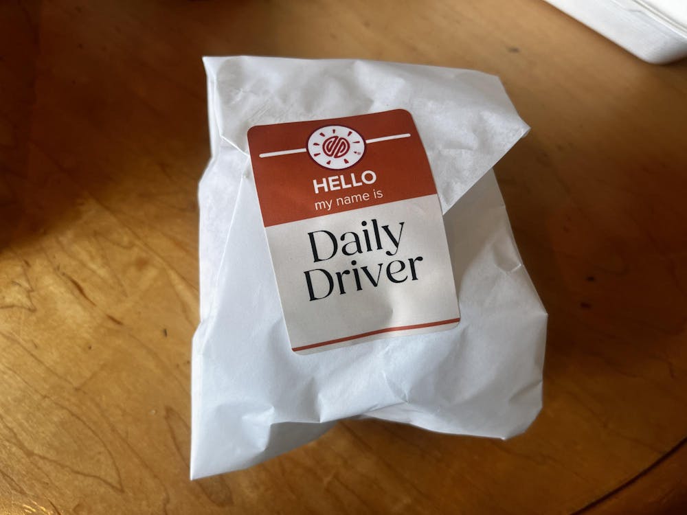 Small World's new burger wrapped in a white package, the red sticker with the Small World Logo reads "HELLO my name is Daily Driver."