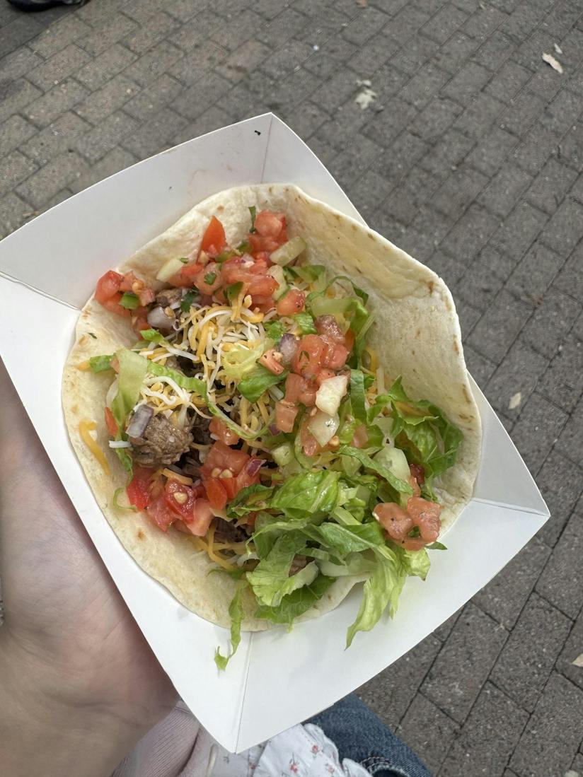 A tortilla filled with guacamole, beef, pico de gallo, lettuce, and cheese sits on a paper plate. 