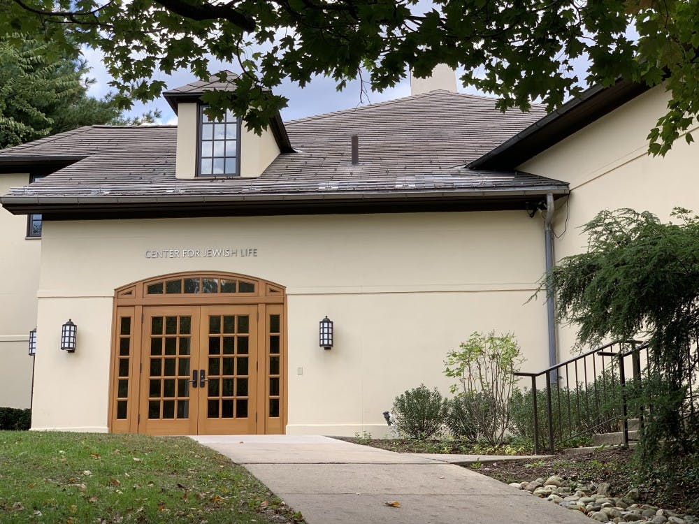 A pale yellow building with a large, windowed door is in the center of the photograph. The words “Center for Jewish Life” are above the door.