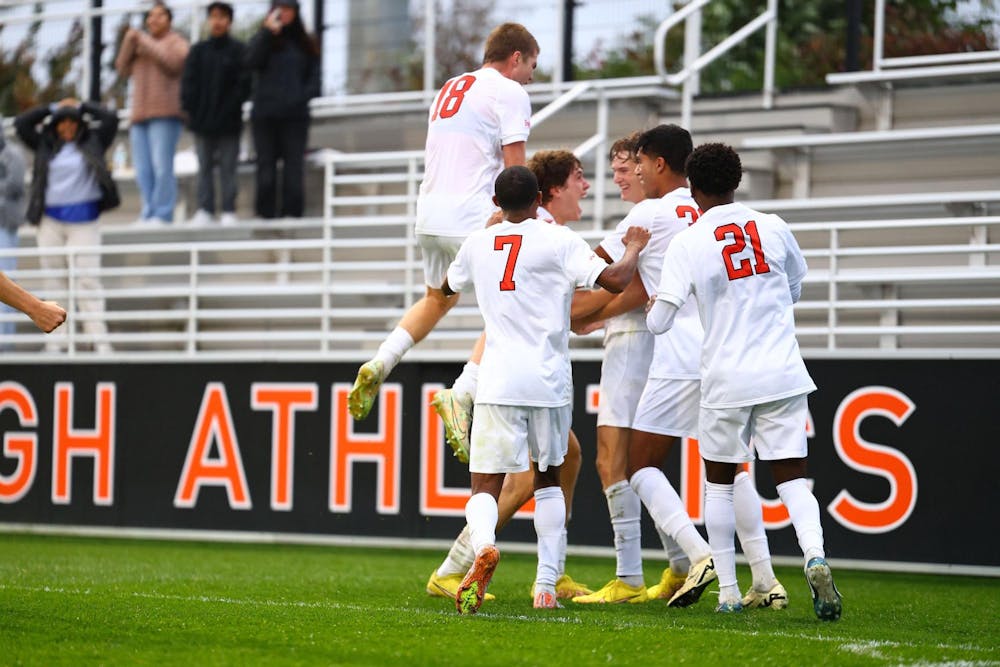 A group of men all wearing white soccer jerseys celebrate on a grass field. 