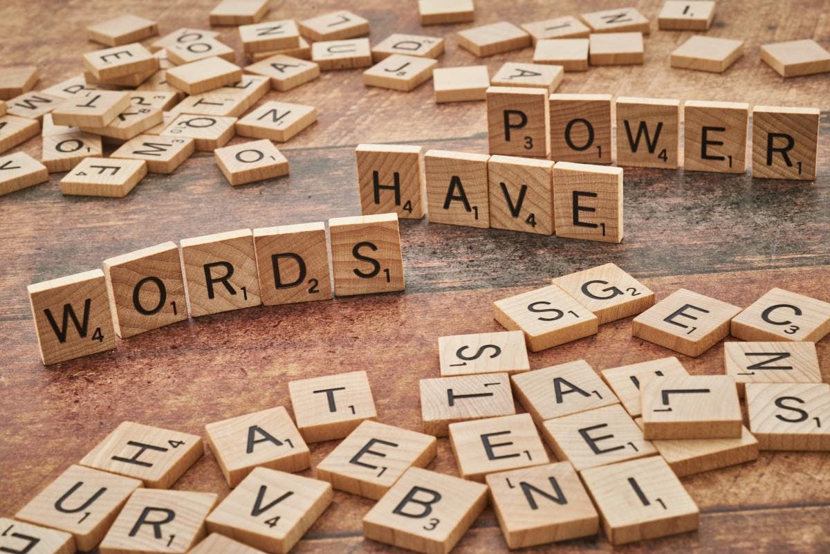Assortment of Scrabble tiles on a wooden table with some standing up spelling out, "WORDS HAVE POWER"