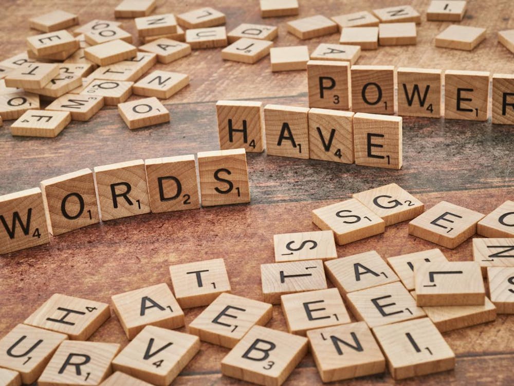 Assortment of Scrabble tiles on a wooden table with some standing up spelling out, "WORDS HAVE POWER"
