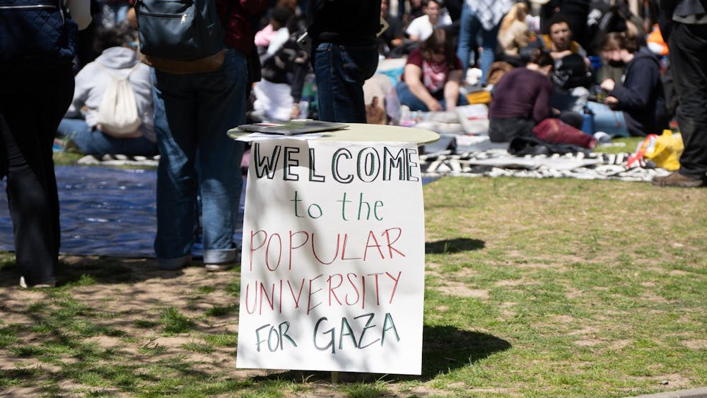 A sign reading “Welcome to the Popular University for Gaza” in black, green, and red letteres on a plain white background.