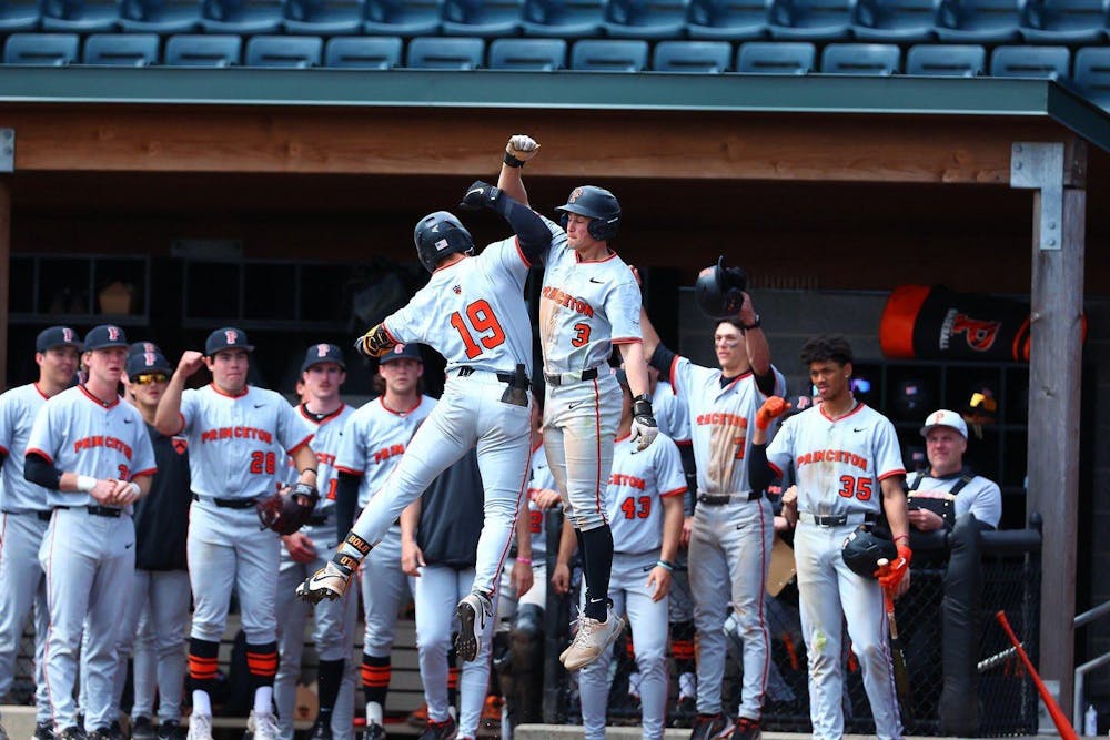Two Princeton players jump and hit elbows in celebration with teammates in dugout behind. 
