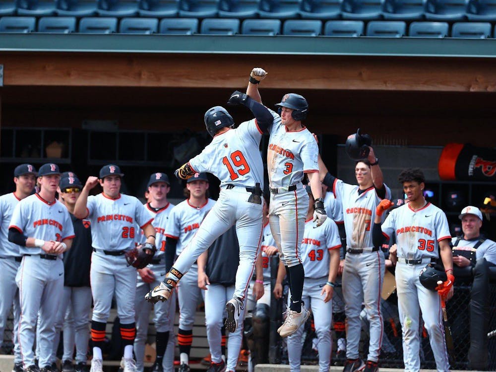 Two Princeton players jump and hit elbows in celebration with teammates in dugout behind. 