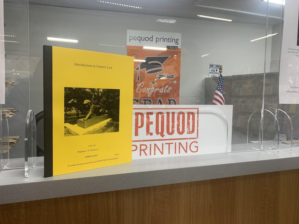 A yellow packet of course material for "Introduction to Islamic Law" resting on a counter next to a sign reading "Pequod Printing"