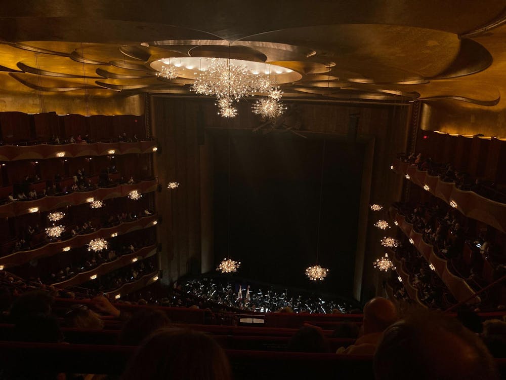 A dark theater with a gold ceiling and chandeliers before the curtains open.