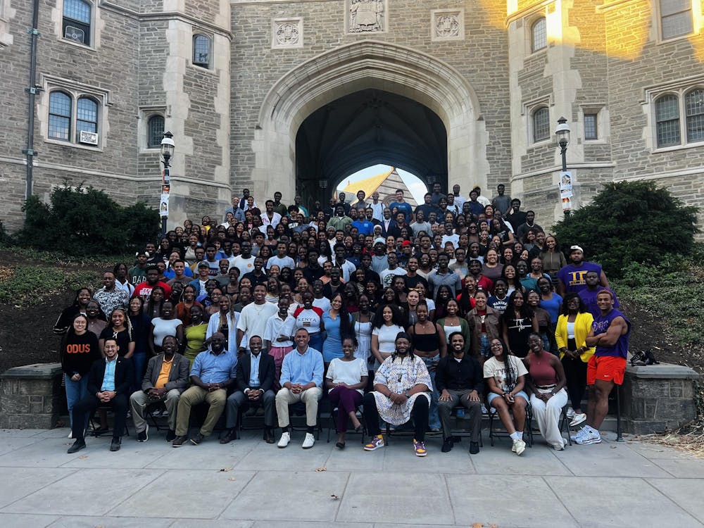 A large group of people pose in rows on a wide set of steps underneath a stone archway