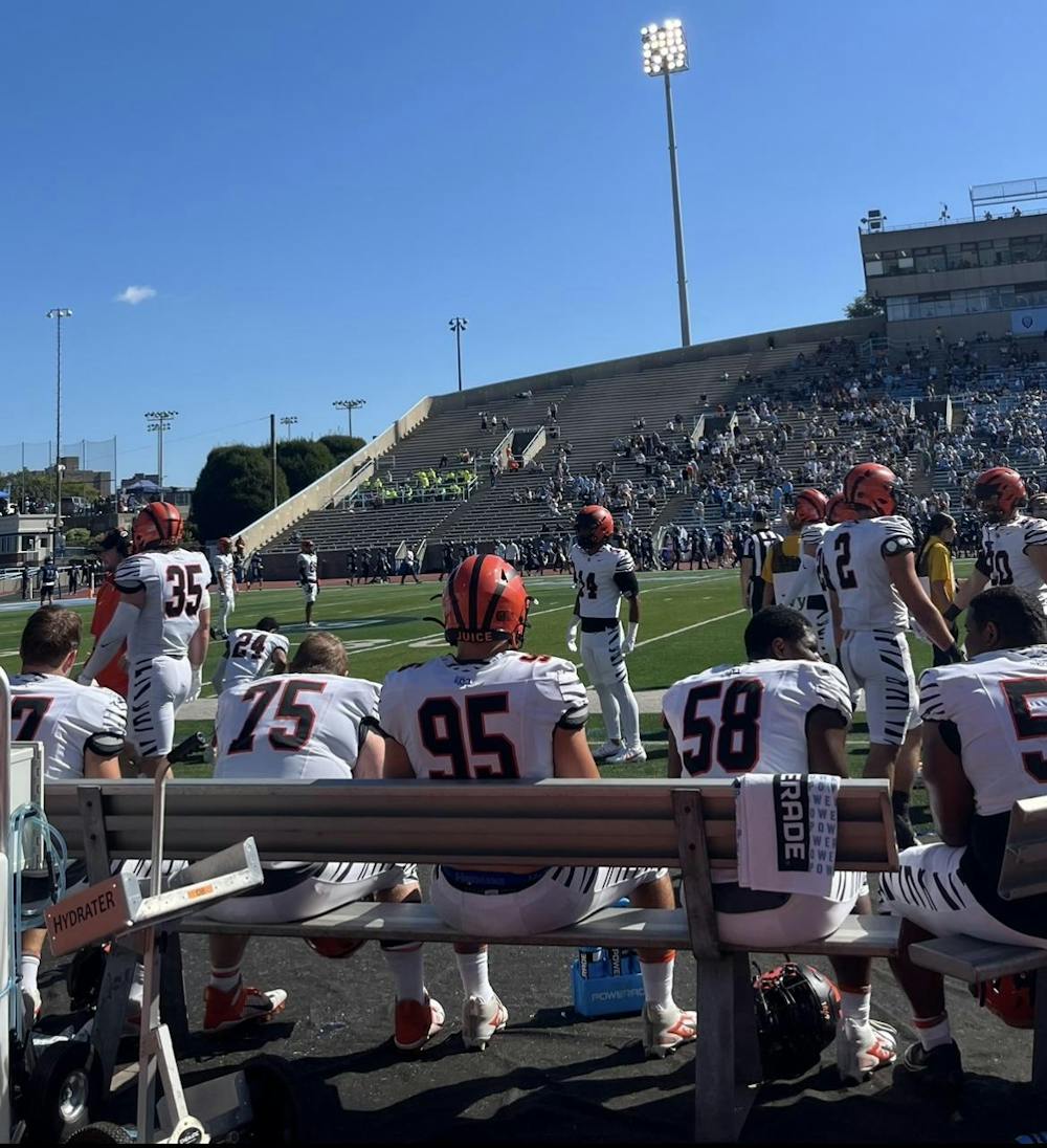 Football players on a bench and on the field, wearing orange and black striped helmets.