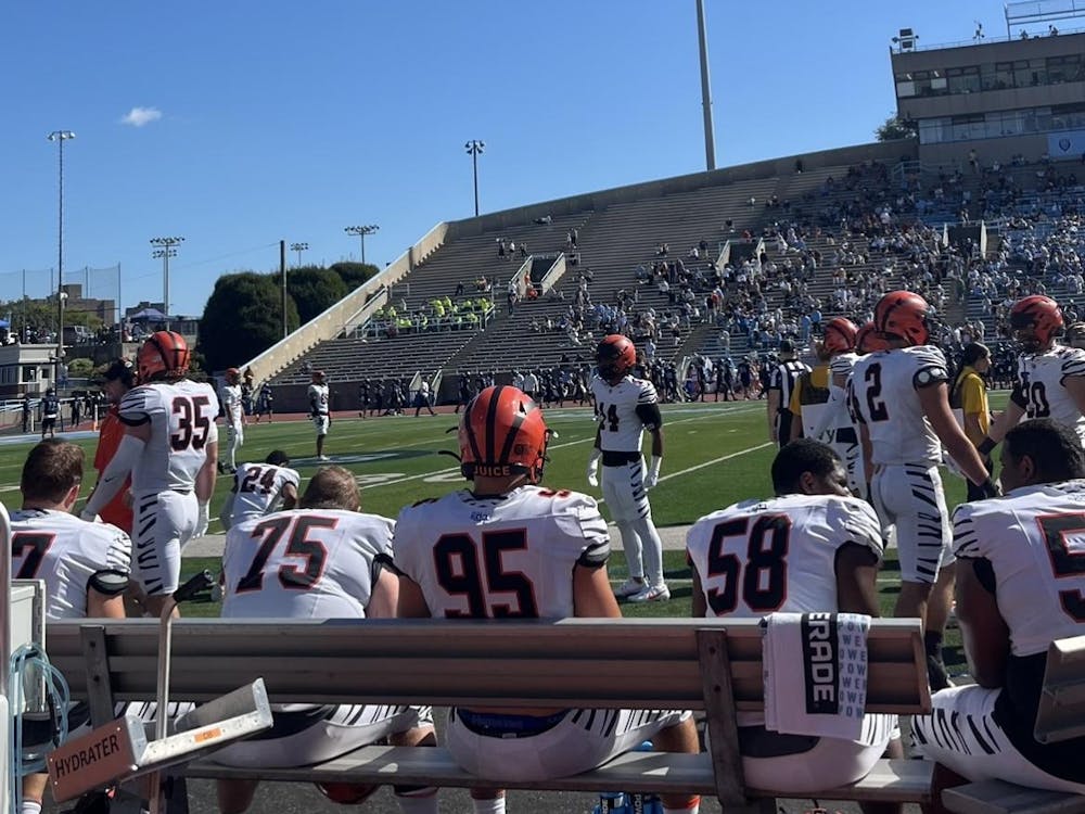 Football players on a bench and on the field, wearing orange and black striped helmets.