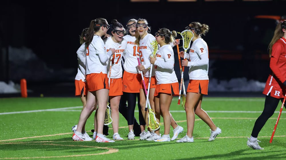 Lacrosse players in orange and white jerseys celebrating together in a group. 