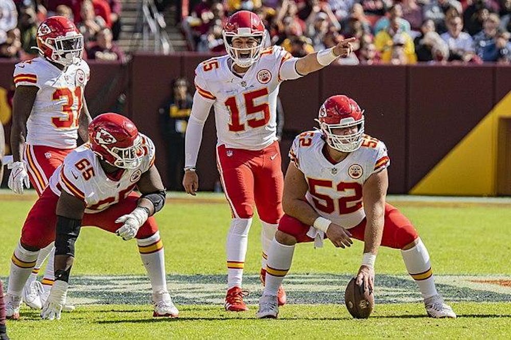 People stand ready to snap and catch football in NFL game.